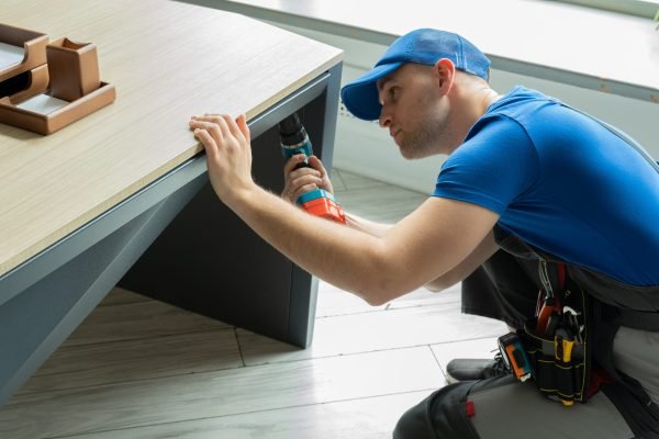Male handyman using an electric screwdriver tool in his hand and repairing a wooden table.